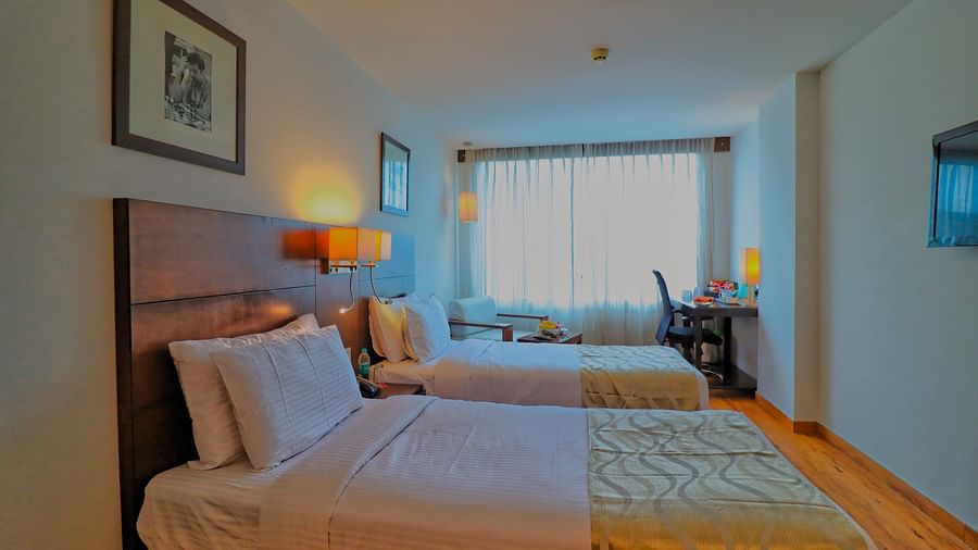A hotel room with two twin beds, a work desk, and a large window with a view -  Clarks Collection, Vadodara